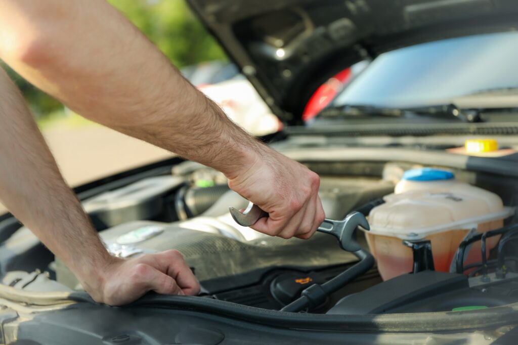 A man holds a wrench over a car engine. Car inspection