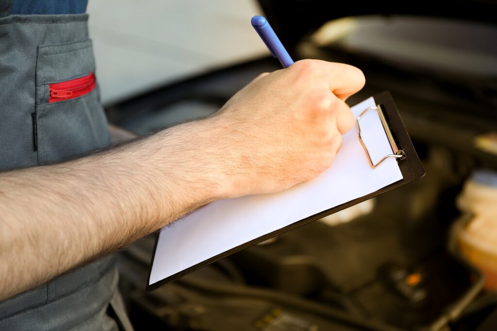 A man in overalls writes to a clipboard. Mechanic. Car inspection